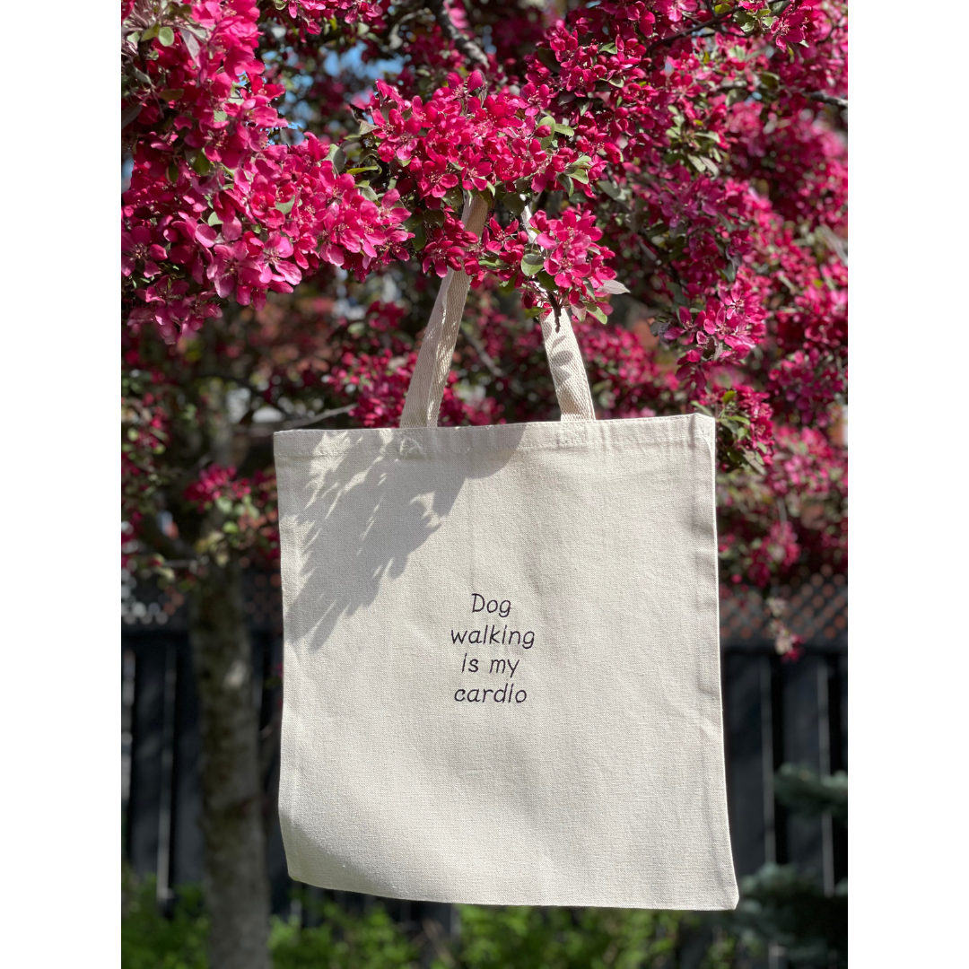 Natural canvas tote bag hung in a tree. Tote bag says "Dogs walking is my cardio"